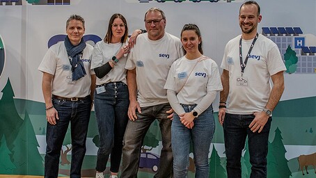 Cinq employés de la SEVJ posent souriants devant le stand du comptoir de la Vallée de Joux, portant des t-shirts avec le logo "SEVJ".