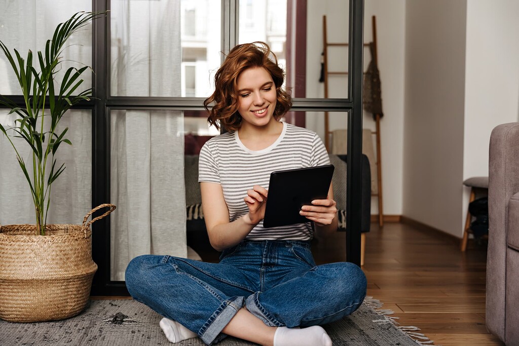 Femme souriante assise chez elle, utilisant sa tablette connectée