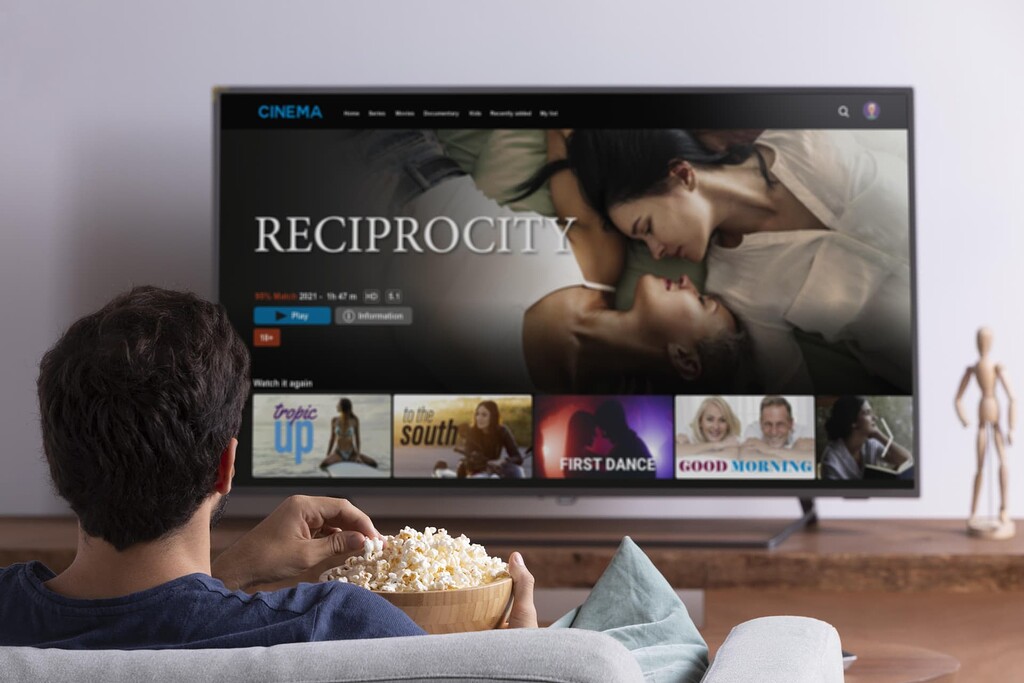 Homme regardant un film sur sa télévision avec Apple TV, tout en mangeant des popcorn dans un plat