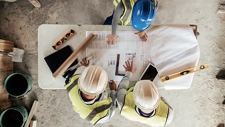 Vue aérienne de 3 personnes avec des casques de chantier, penchés sur un plan