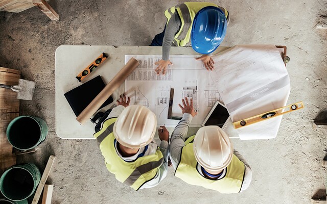 Vue aérienne de 3 personnes avec des casques de chantier, penchés sur un plan