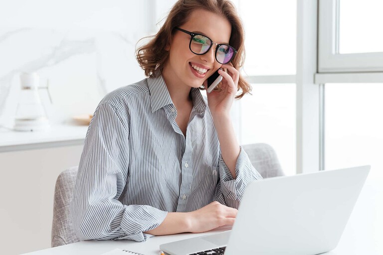 Jeunes femmes avec des lunettes, passant un appel en étant devant son ordinateur portable