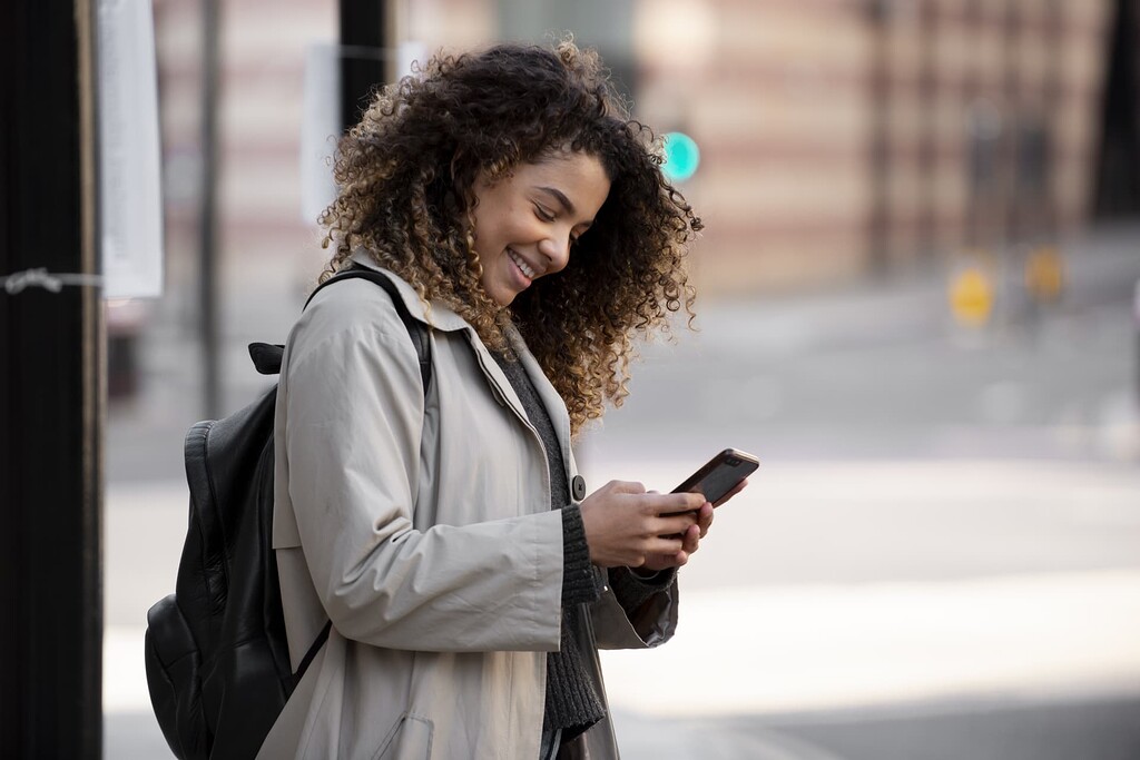 Femme dans la rue consultant son téléphone, le sourire au lèvres