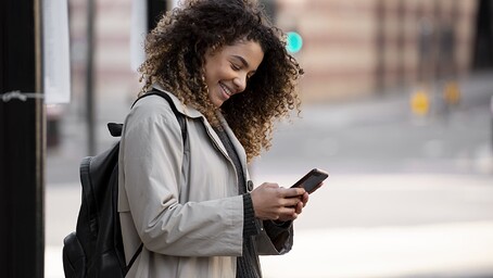 Femme dans la rue consultant son téléphone, le sourire au lèvres